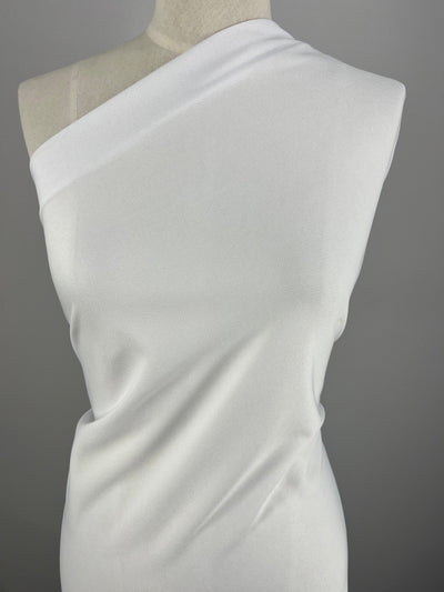 A dress form is wearing a one-shoulder white dress made of smooth, slightly textured polyester fabric from Super Cheap Fabrics. The minimalist design features a draped fit, perfectly showcased against a plain gray background. The fabric used is the Lacoste - White - 150cm.
