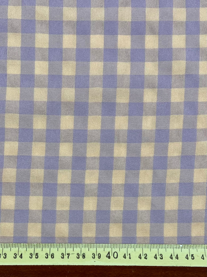 Fabric with a peach and purple checkered pattern. The bottom of the image features a light green measuring tape showing measurements from 37 to 45 inches. This lightweight fabric is perfect for various crafting projects. Introducing Cotton Poly - Peach & Purple Gingham - 150cm from Super Cheap Fabrics!