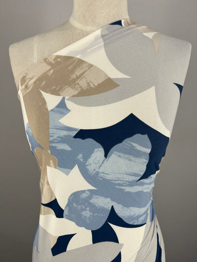 A mannequin dressed in a sleeveless, asymmetrical top crafted from medium-weight Polyester/Spandex fabric with a large floral pattern in shades of blue, white, and beige stands against a neutral gray background using Super Cheap Fabrics' Printed Lycra - Flower Projection - 150cm.