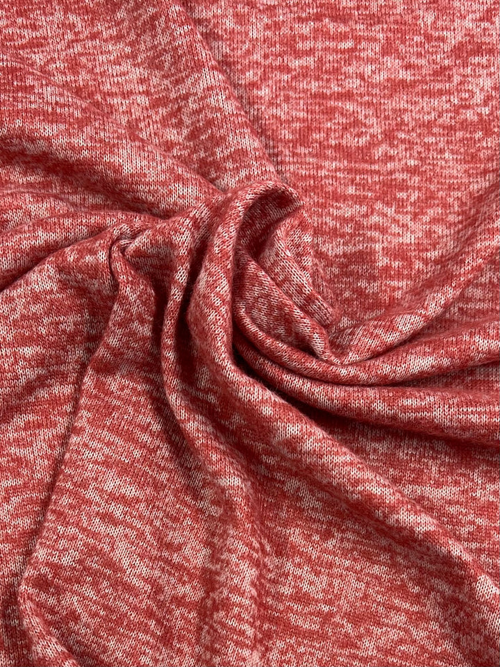 A close-up view of a piece of fabric with a red and white mottled pattern, showing a soft and slightly textured surface. The medium-weight fabric is gathered in folds and creases, capturing the detail and drape of the Marle Textured Knit - Burnt Ochre - 160cm by Super Cheap Fabrics.
