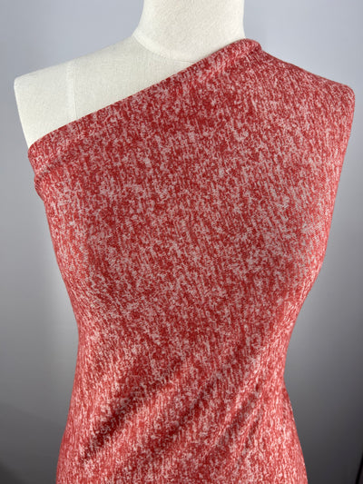 A close-up of a red and white textured dress on a dress form. The dress has a one-shoulder design, revealing the left shoulder and covering the right. Crafted from Marle Textured Knit - Burnt Ochre - 160cm from Super Cheap Fabrics, the heathered medium weight fabric offers both a casual yet chic appearance with generous stretch for comfort.