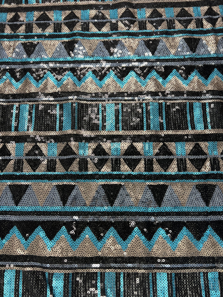 A close-up of the Designer Sequins- Stripe Zag - 150cm by Super Cheap Fabrics, showcasing a mesh fabric pattern with horizontal rows of geometric shapes in metallic sequins. The pattern features triangles, zigzags, and stripes in shades of black, silver, gray, blue, and teal, creating a vibrant and textured design perfect for dance wear.