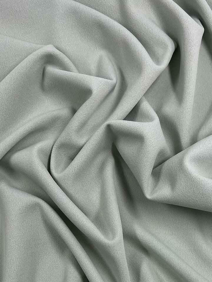 A close-up of Super Cheap Fabrics' Plain Scuba Crepe - Sea Foam - 160cm with gentle folds and creases, creating a textured and wavy appearance. The fabric's surface has a subtle, smooth texture, adding depth and dimension to the image.