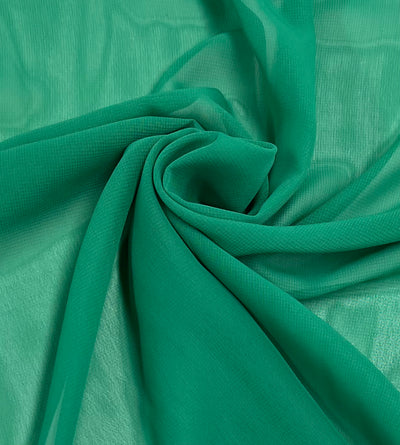 A close-up image of a piece of Hi-Multi Chiffon - Green Tambourine - 150cm by Super Cheap Fabrics. The fabric is gathered and swirled into a circular pattern, showcasing its soft, lightweight, and somewhat sheer texture—perfect for creating elegant floaty tops.