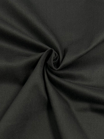 A close-up image of Super Cheap Fabrics' Cotton Sateen - Black - 148cm with a smooth texture, twisted into a central spiral formation. The medium-weight material appears soft and slightly shiny, likely wrinkle-resistant.