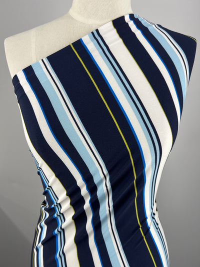 A close-up of a one-shoulder dress on a mannequin. The dress, made from medium weight polyester spandex, features diagonal stripes in navy blue, white, light blue, yellow, and black. The form-fitting material boasts a smooth one way stretch, accentuating the curves of the mannequin. The fabric used is Printed Lycra - Ocean Stripe by Super Cheap Fabrics.