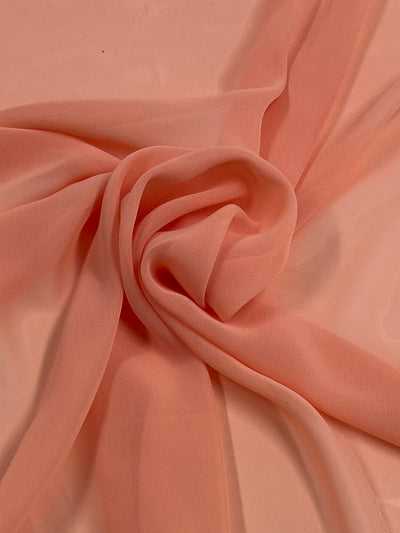 A close-up view of Hi-Multi Chiffon - Powder Peach - 150cm from Super Cheap Fabrics arranged in soft folds and swirls, creating a delicate and elegant appearance. This lightweight fabric has a gentle sheen, akin to those used for floaty tops, making it appear both airy and sophisticated.