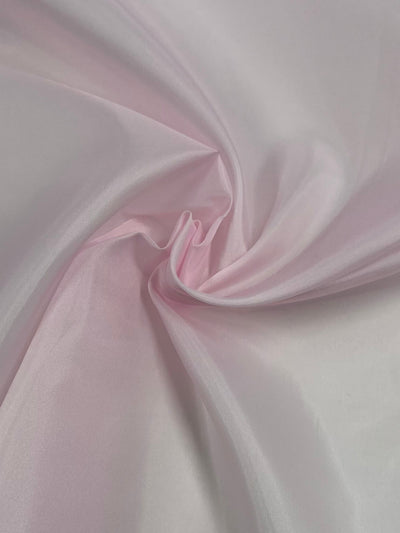 A close-up of Super Cheap Fabrics' Lining - Light Pink - 150cm with gentle folds and a soft texture. The lightweight fabric is arranged in a way that creates smooth waves and a subtle, elegant drape.