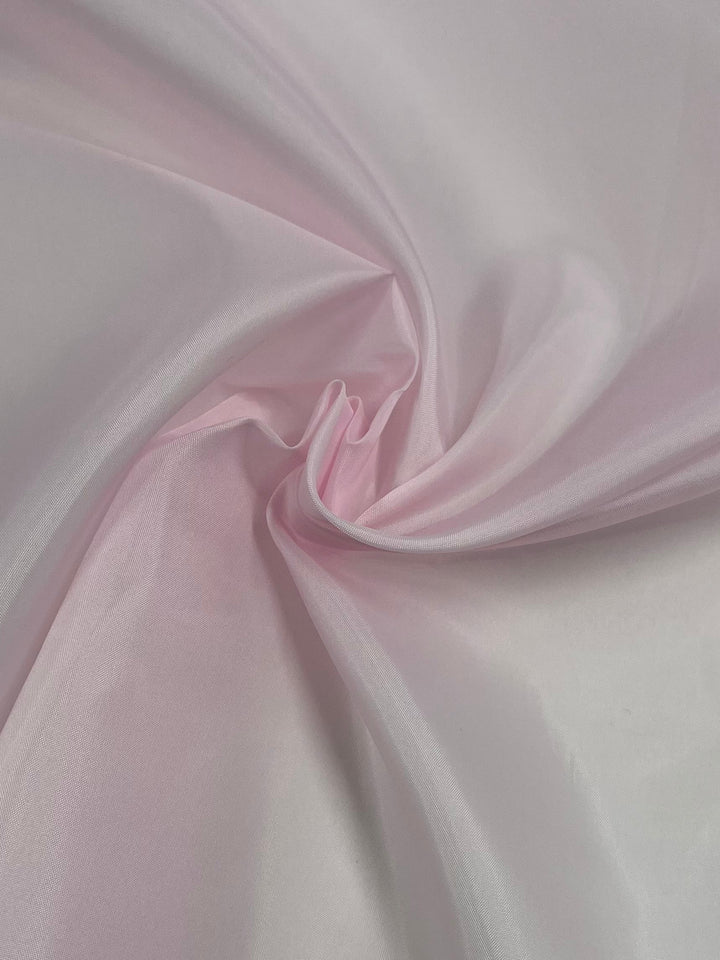 A close-up of Super Cheap Fabrics' Lining - Light Pink - 150cm with gentle folds and a soft texture. The lightweight fabric is arranged in a way that creates smooth waves and a subtle, elegant drape.