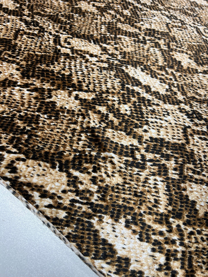 Close-up of Super Cheap Fabrics' Printed Velvet - Python, a light to medium weight polyester with brown and black snakeskin pattern, detailed scales and texture on a light background. Fabric width: 150cm.