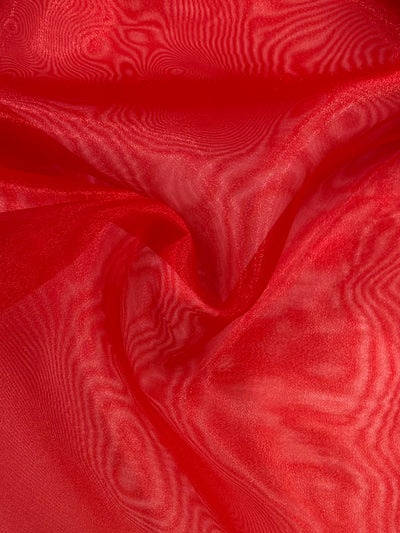 A close-up of the Organza - Red - 150cm fabric by Super Cheap Fabrics, showcasing its soft, elegantly draped texture with a slightly sheer finish. The light plays across the surface, creating delicate patterns and highlighting the smooth folds and vibrant hue.