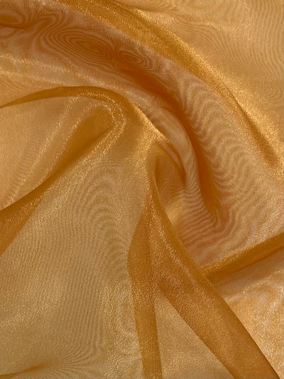 A close-up view of delicate, sheer Organza - Gold - 150cm from Super Cheap Fabrics in a warm golden-orange hue. The fabric appears to be soft and lightweight, with gentle folds and a subtle shimmer, creating an elegant and flowing texture.
