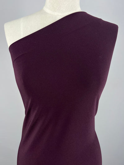 A mannequin dressed in a one-shoulder, deep wine color ITY Knit - Wine - 150cm from Super Cheap Fabrics against a plain gray background. The polyester spandex fabric is smooth and form-fitting, highlighting the mannequin's shape.