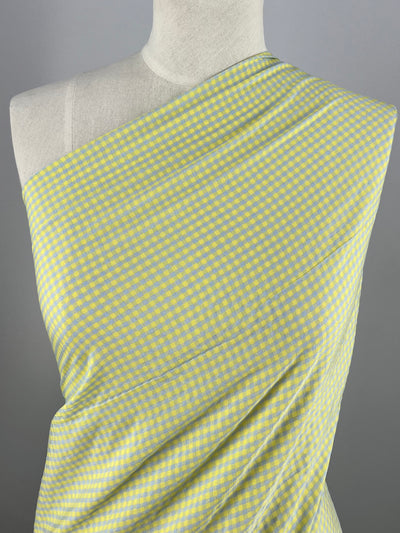 Image of a mannequin dressed in a one-shoulder garment made of light-weight fabric with a blue and yellow checkered pattern. The Super Cheap Fabrics Cotton Poly - Mini Gingham Blue & Yellow- 150cm material drapes smoothly over the mannequin's upper body, showcasing the intricate, close-knit design and vibrant colors.