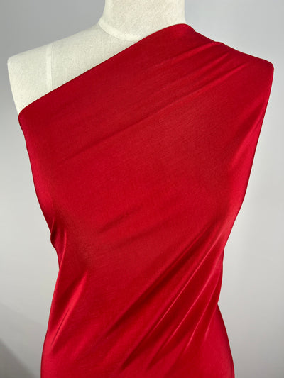 A mannequin dressed in a vibrant red, Microfibre - Urban Red - 150cm from Super Cheap Fabrics that drapes elegantly across the torso against a plain gray background. The lightweight fabric appears smooth and slightly stretchy, showcasing the vibrant color and texture.