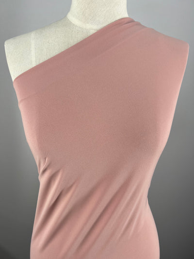 A dress mannequin is draped in a soft, Bridal Rose one-shoulder garment made from ITY Knit - Bridal Rose - 150cm by Super Cheap Fabrics. The medium weight fabric appears smooth and slightly stretchy, fitting snugly around the form. The backdrop is a neutral grey.