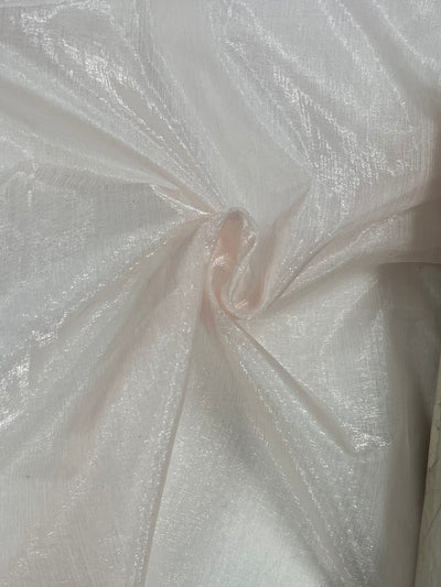 A close-up of shimmery, sheer Super Cheap Fabrics' Organza - Mauve Chalk - 150cm with a soft texture, gently gathered in the middle. The lightweight fabric appears to be light in color, possibly white or pale pink, and has a subtle sheen that reflects light.